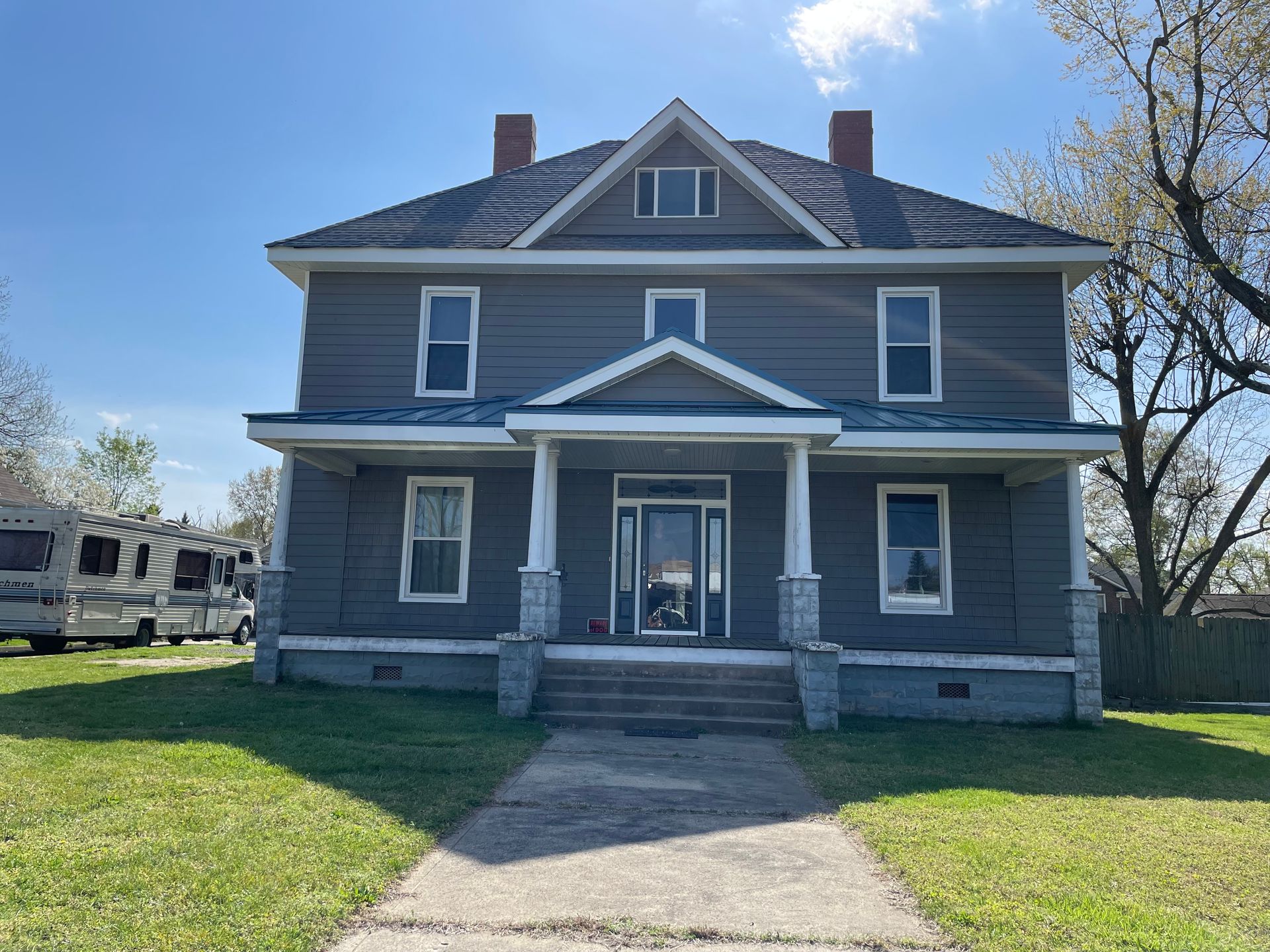 A large gray house with a porch and a trailer parked in front of it.