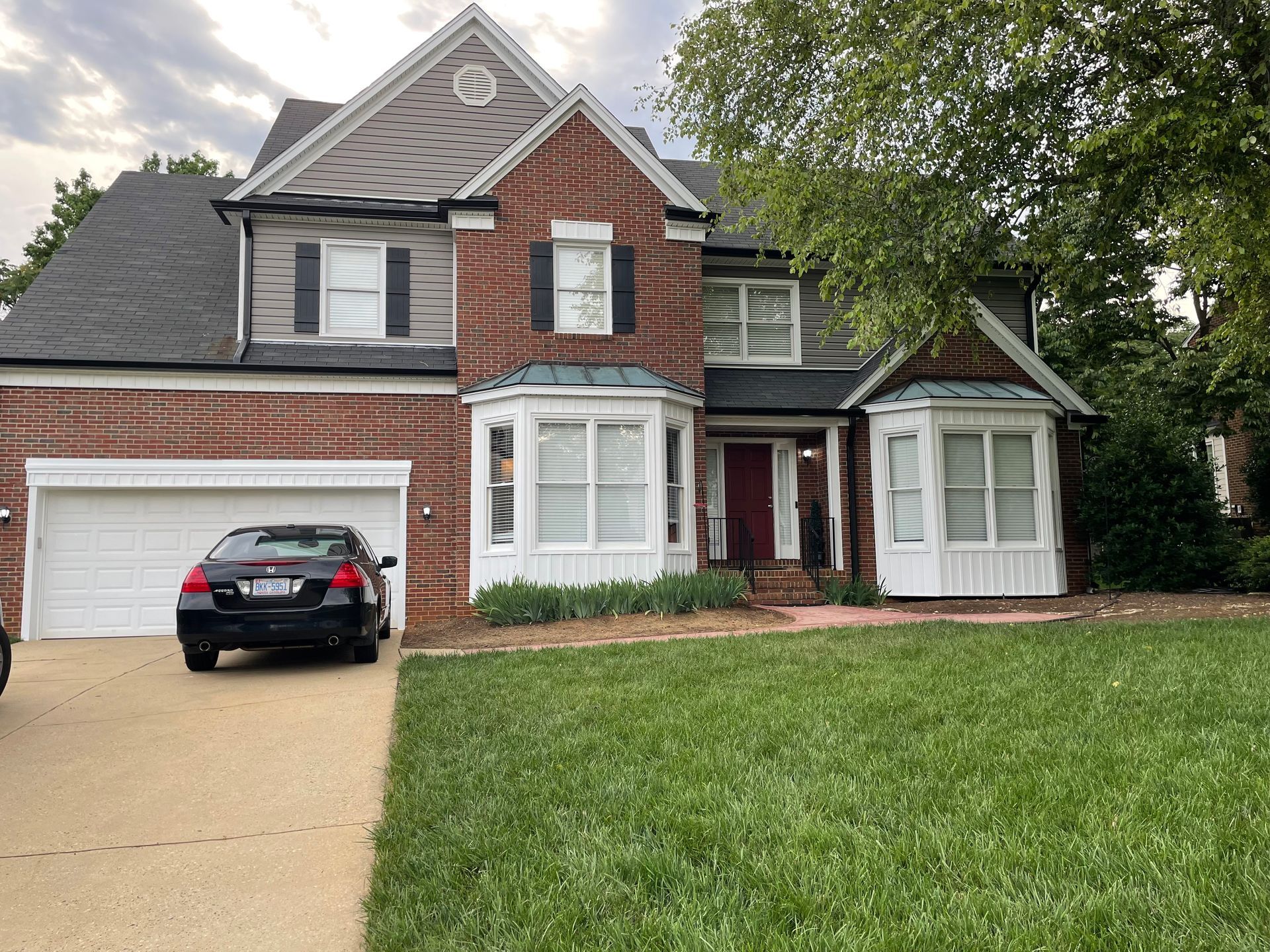 A car is parked in front of a large brick house.