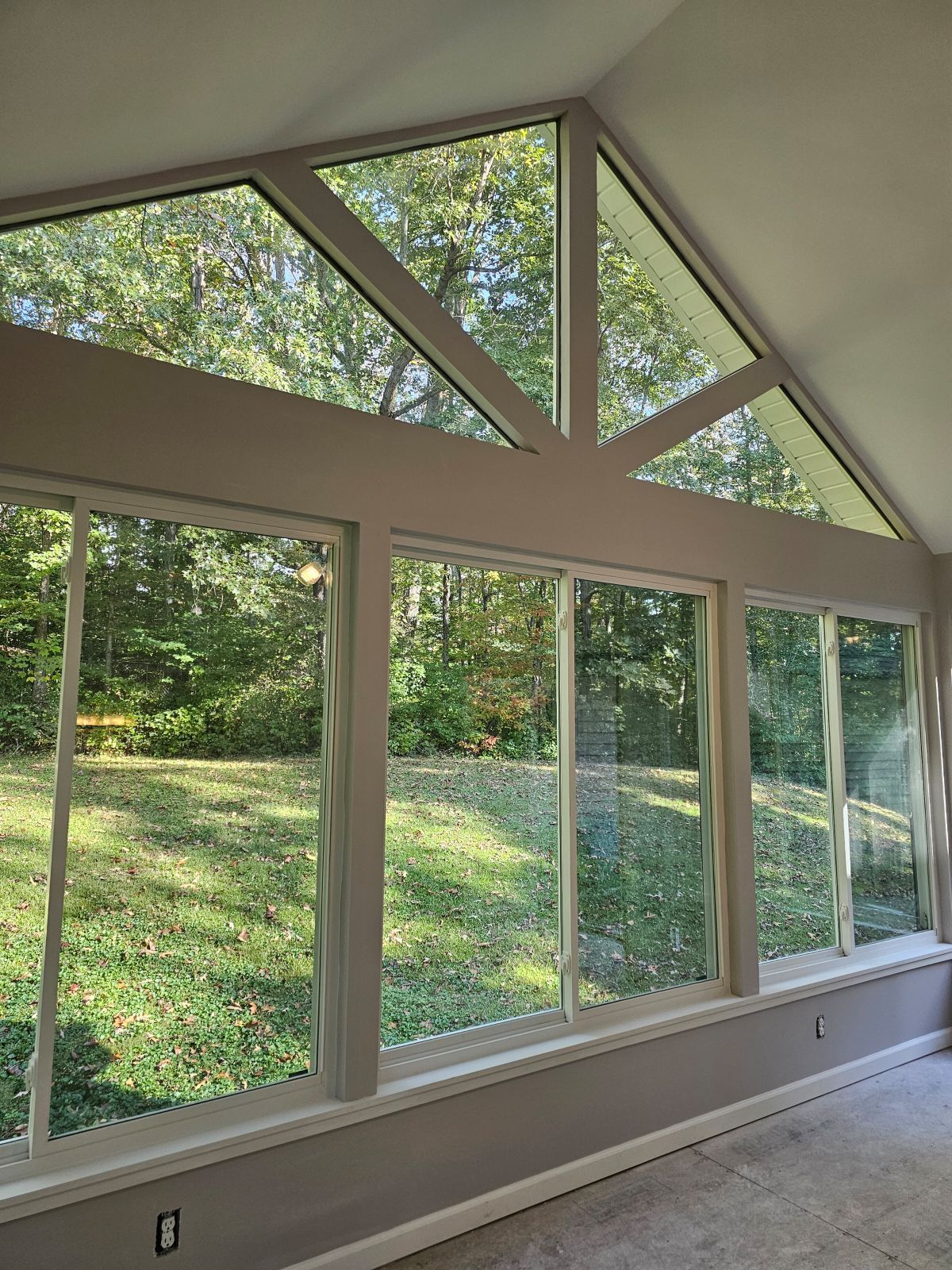 A room with a lot of windows and a view of a forest.