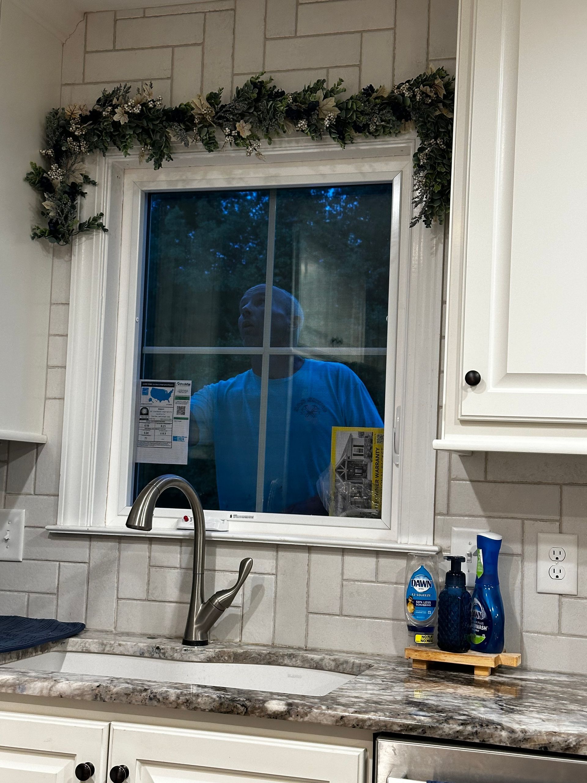 A man is looking out of a window in a kitchen.