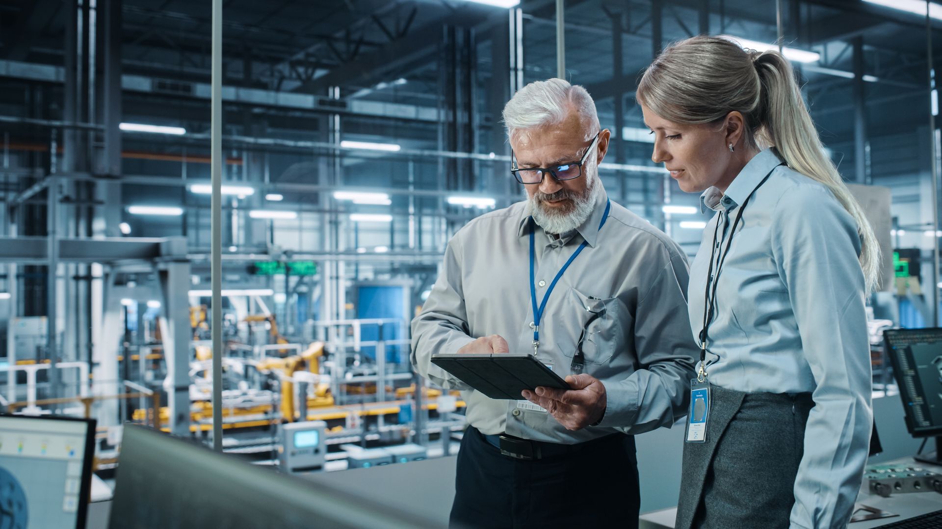 A man and a woman are looking at a tablet in a factory.