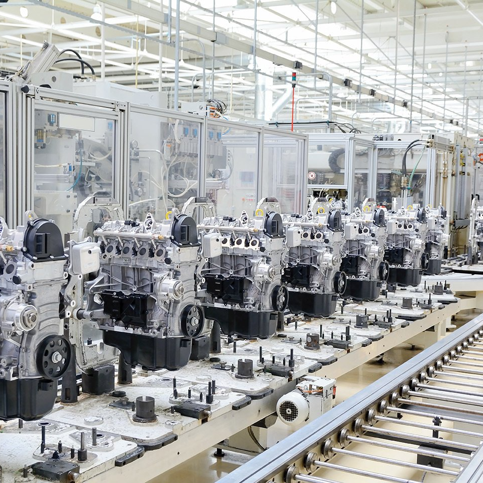 A row of engines are sitting on a conveyor belt in a factory.