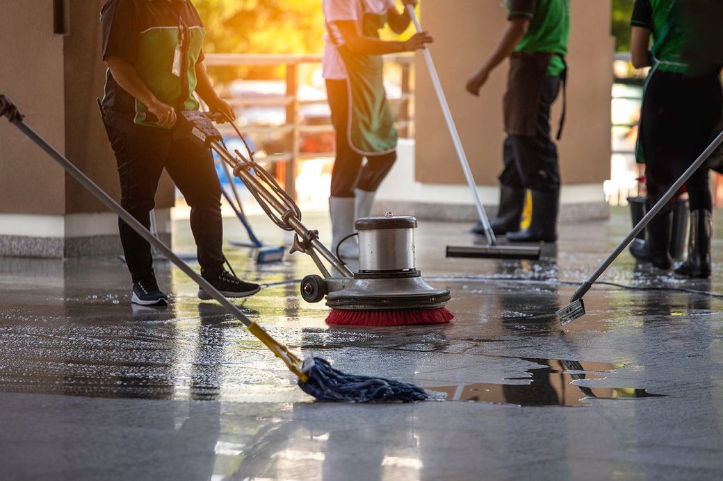 Workers cleaning a wet floor with floor buffers and mops in a bright indoor space
