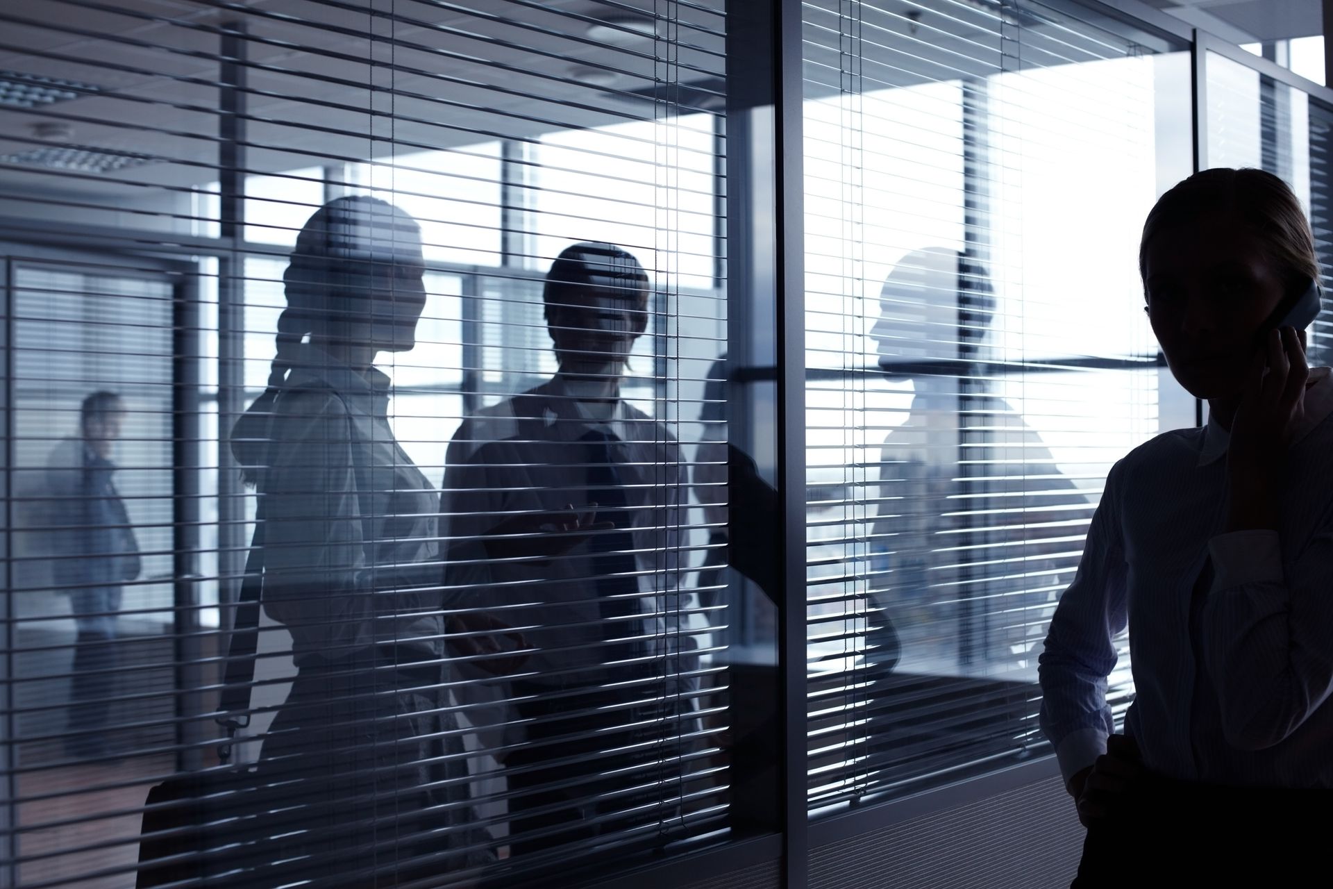 People reflected in glass office walls; some talking on the phone, others blurred in the background.