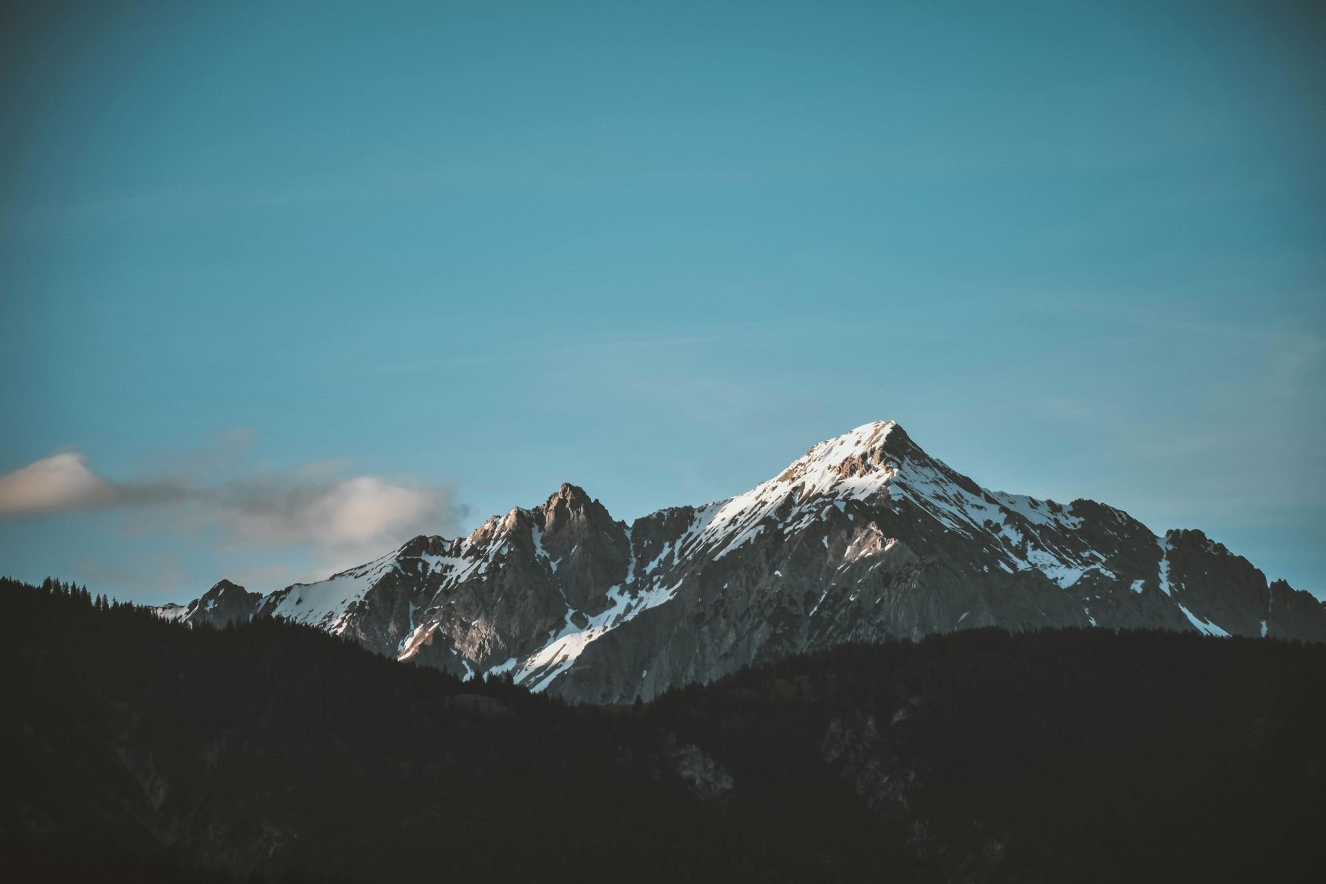 Snow-capped mountains against a clear, blue sky. Dark silhouetted hills in the foreground.
