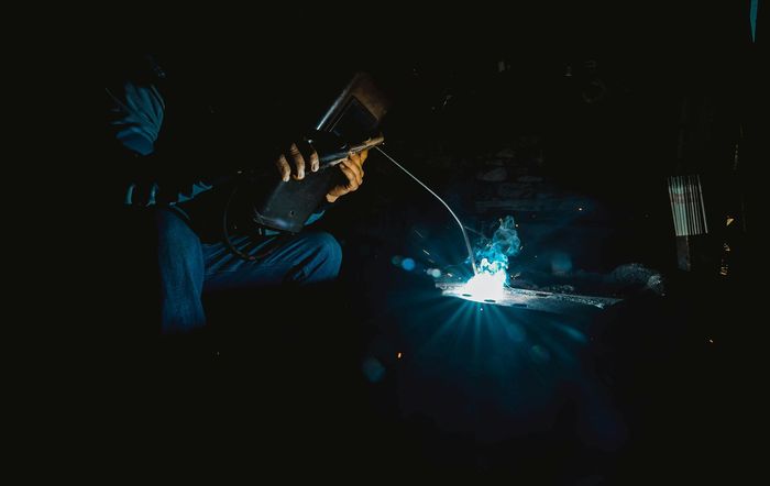 A man is welding a piece of metal in a dark room.