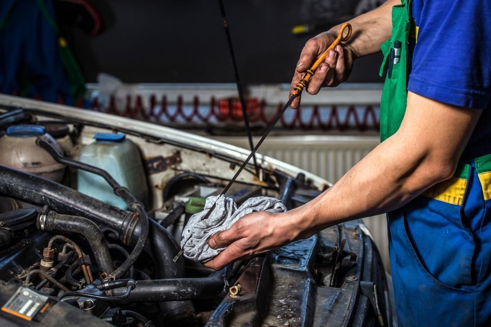 A Man is Checking the Oil Level of a Car With an Oil Dipstick — Bob Parkes Automotive in Hyde Park, QLD