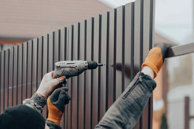 A man is using a drill to install a metal fence.