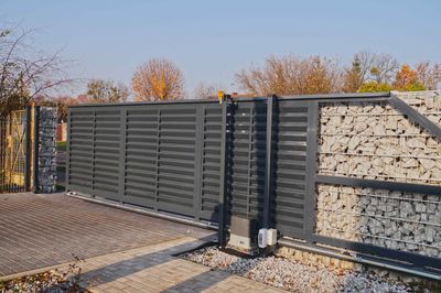 A sliding gate with a motor attached to it is surrounded by a stone wall.