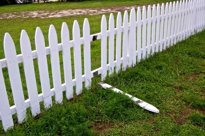 A white picket fence is in the middle of a lush green field.