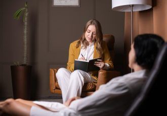 Un terapeuta toma notas mientras conversa con un paciente en un entorno de oficina cómodo.