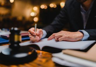 Una persona con traje escribe en un libro con un mazo sobre la mesa, probablemente en un entorno legal.