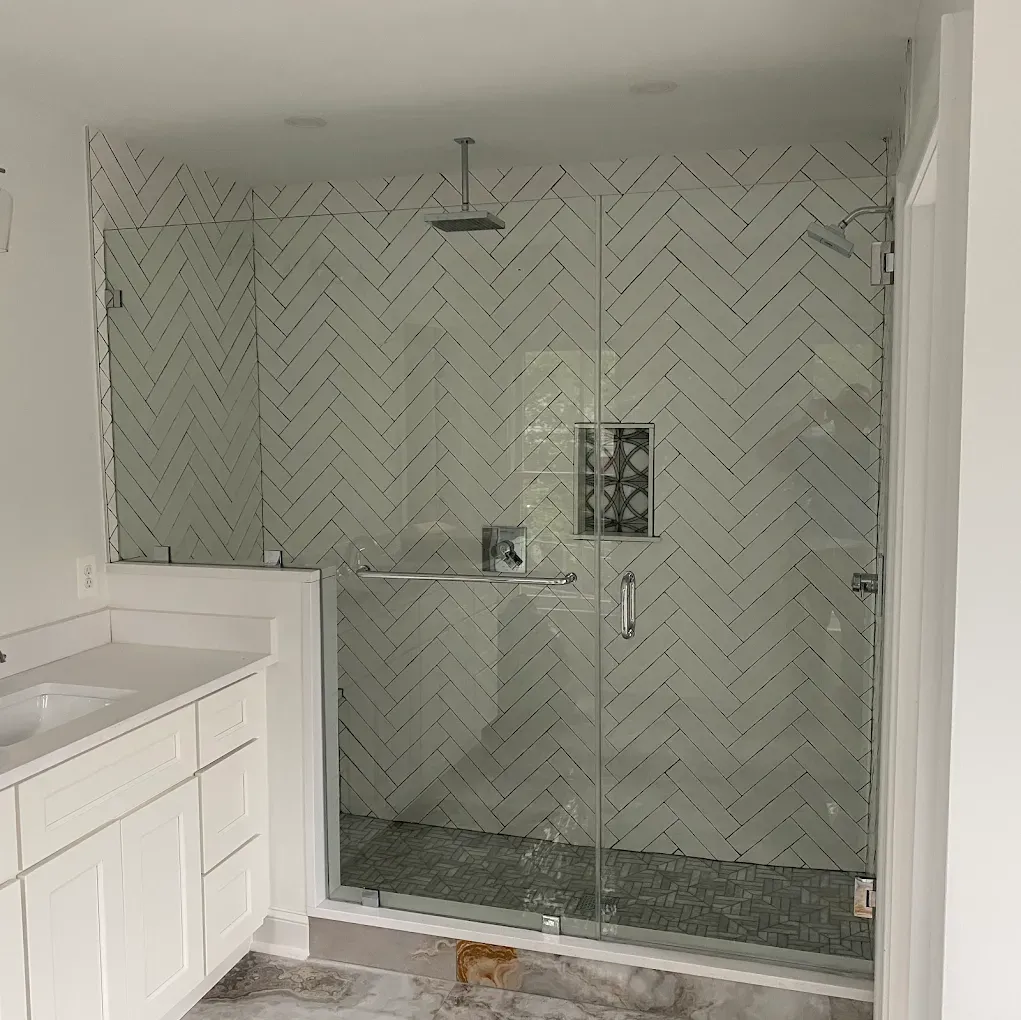 Bathroom with herringbone tile shower, glass doors, silver fixtures, and white vanity.