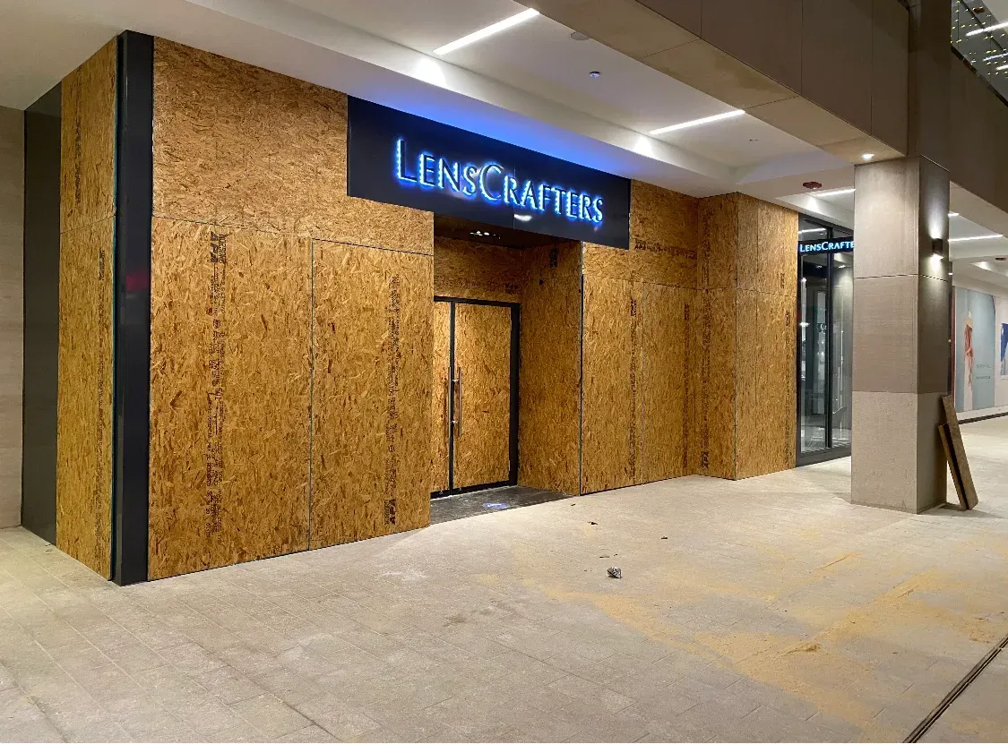 A LensCrafters store under construction. The storefront is covered in wood panels with a blue sign.