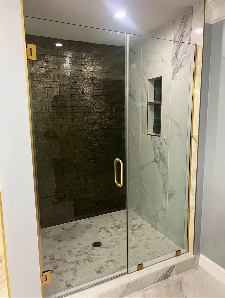 Glass shower with gold trim. Features dark brick accent wall, marble tile, and a built-in shelf.