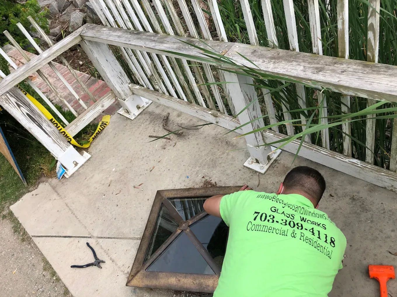 Man in green shirt working on a window frame near a deck with white railing.