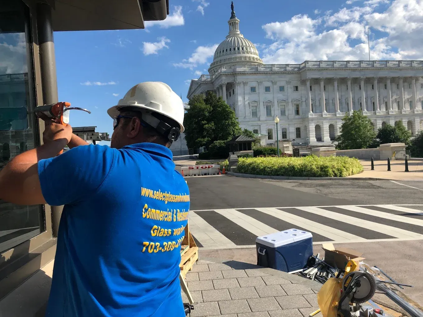 Man in blue shirt and hard hat works near the US Capitol building.