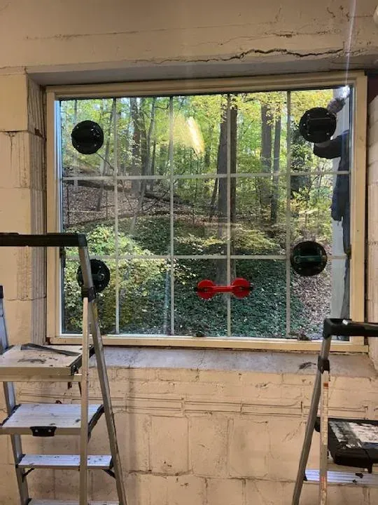 Window replacement with suction cups, overlooking a forest; ladders on either side.