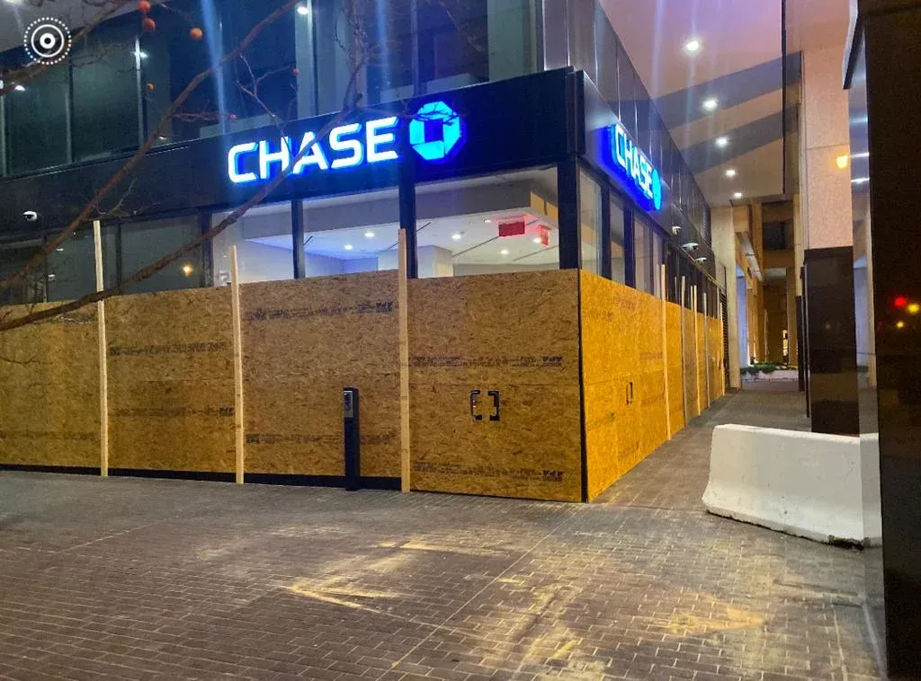 Chase bank storefront boarded up with plywood at night.