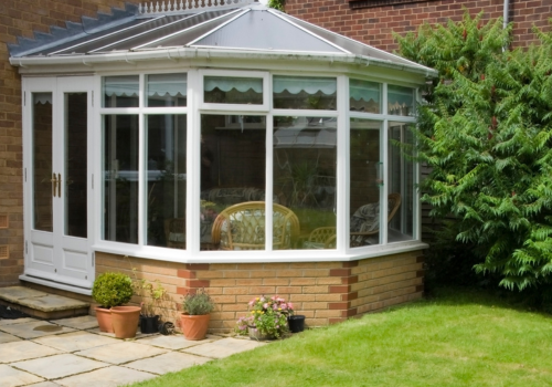 A white conservatory is sitting in the backyard of a brick house.