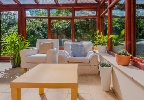 A living room with a table , chairs and potted plants in a conservatory.
