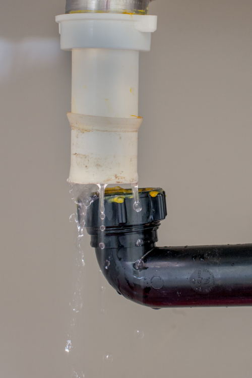 Water is leaking from a broken pipe under a sink.