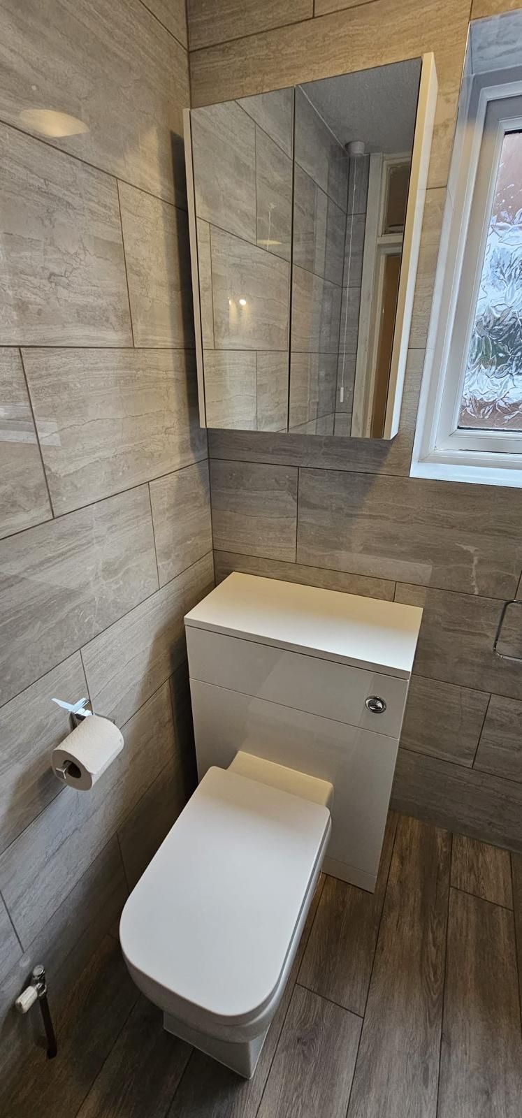 A bathroom with a toilet , sink , mirror and window.