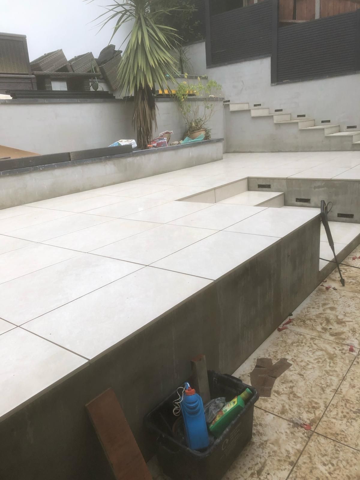 A bucket of cleaning supplies sits on a tiled patio next to stairs.