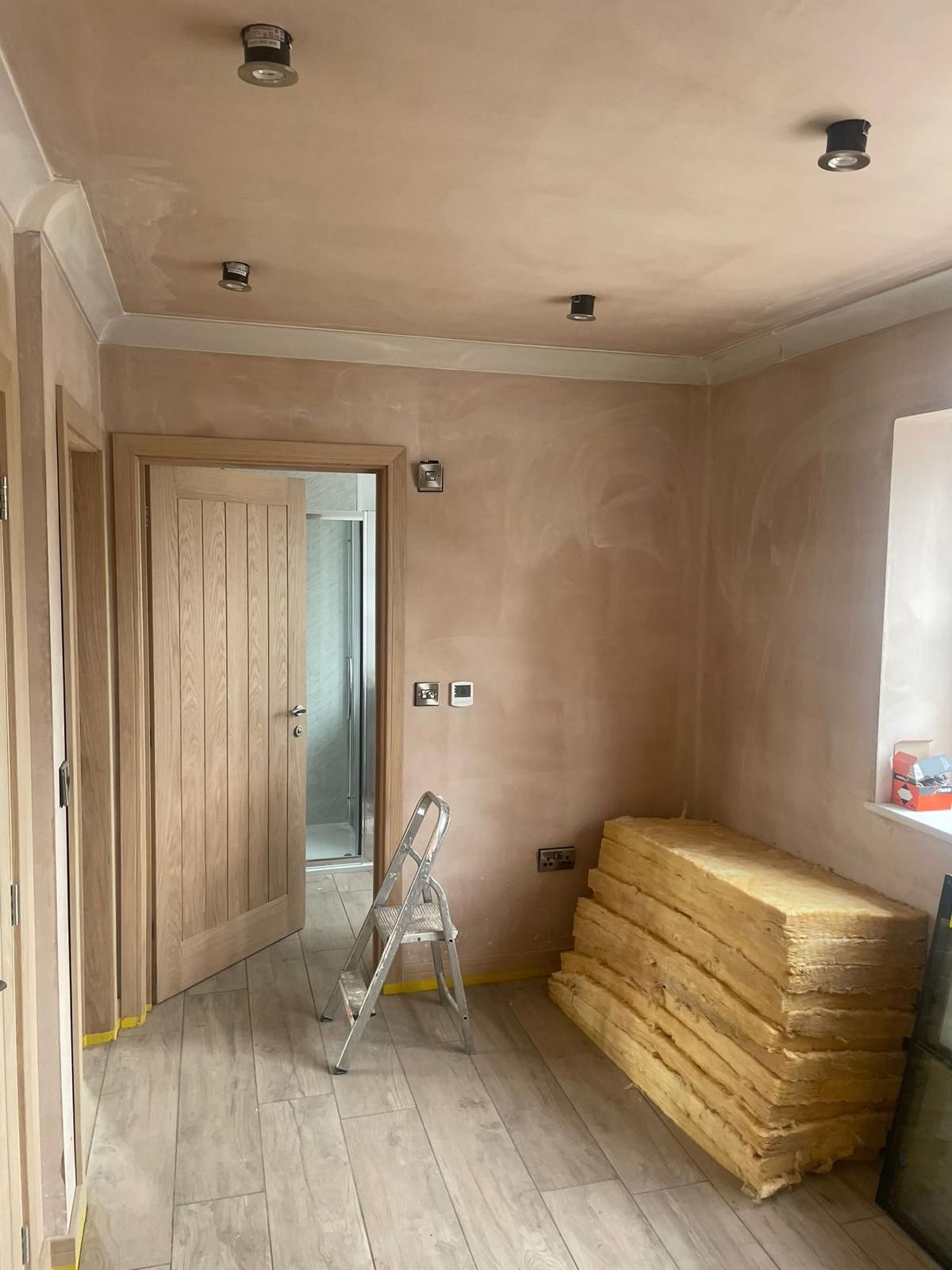 A room with a ladder and a stack of insulation on the floor.