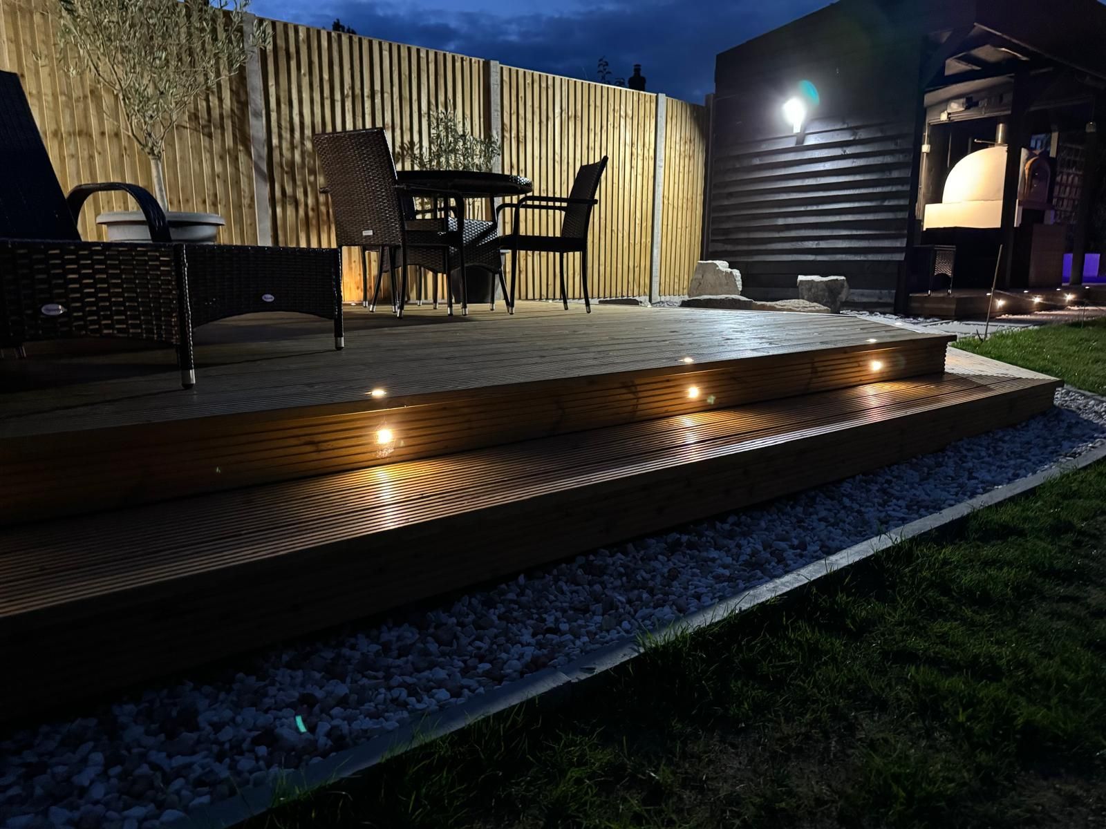 A deck with a table and chairs is lit up at night.