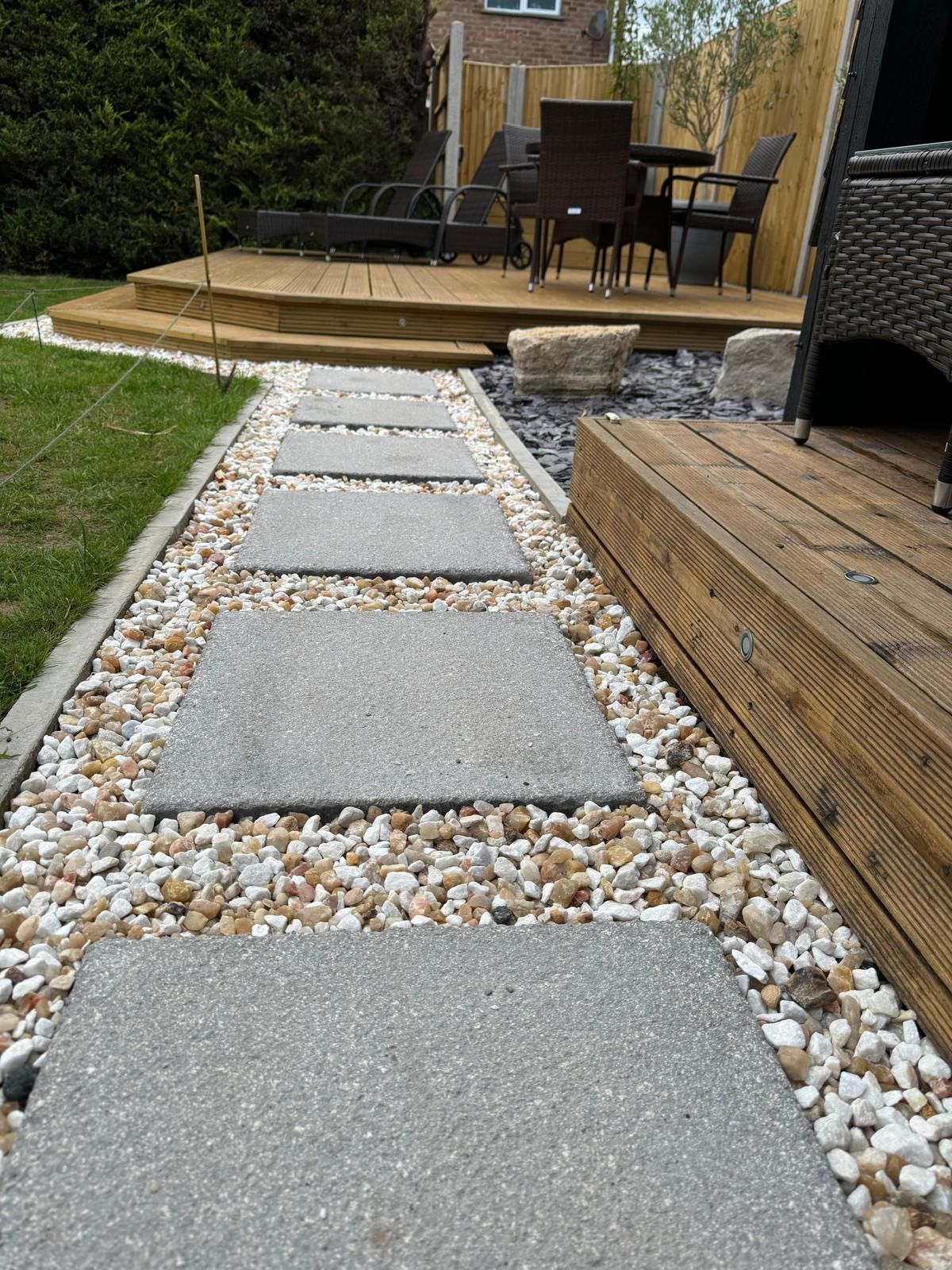 A stone walkway leading to a deck with a table and chairs.