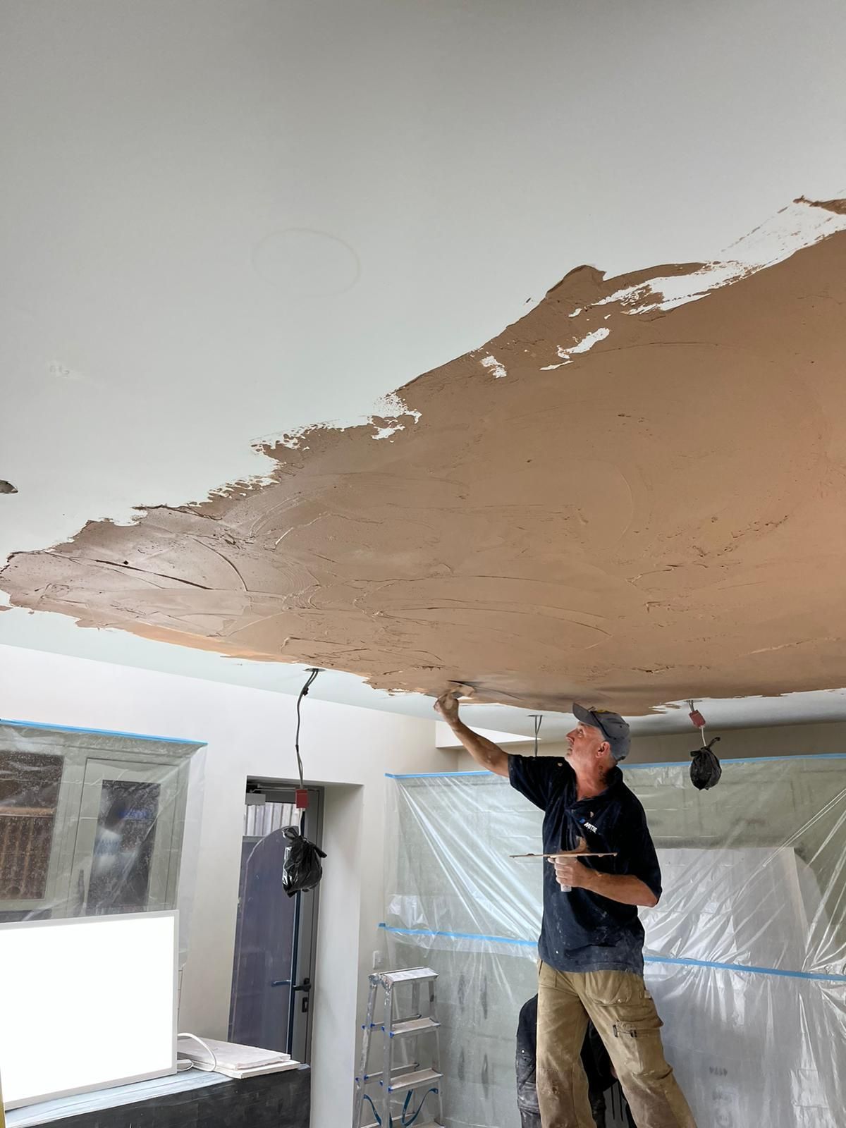 A person is painting a wall with a spatula and brush.