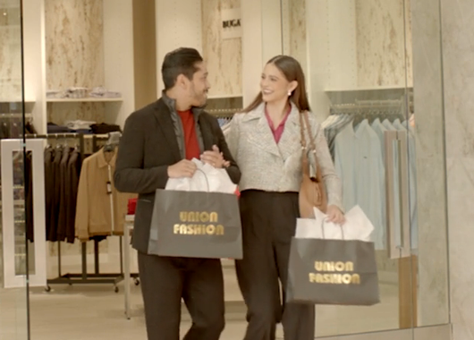 A man and a woman are walking through a store holding bags that say union fashion.