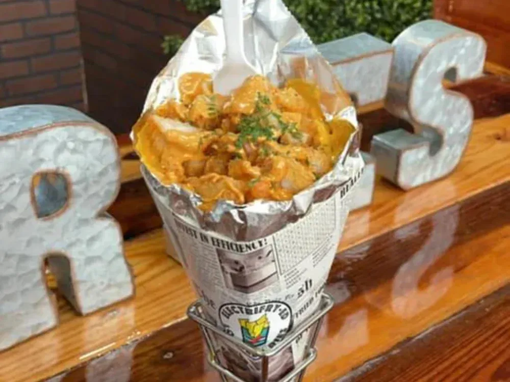 A cone filled with food and a spoon is sitting on a wooden table.