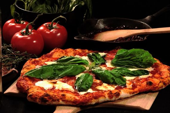 A pizza with basil and cheese is on a wooden cutting board.