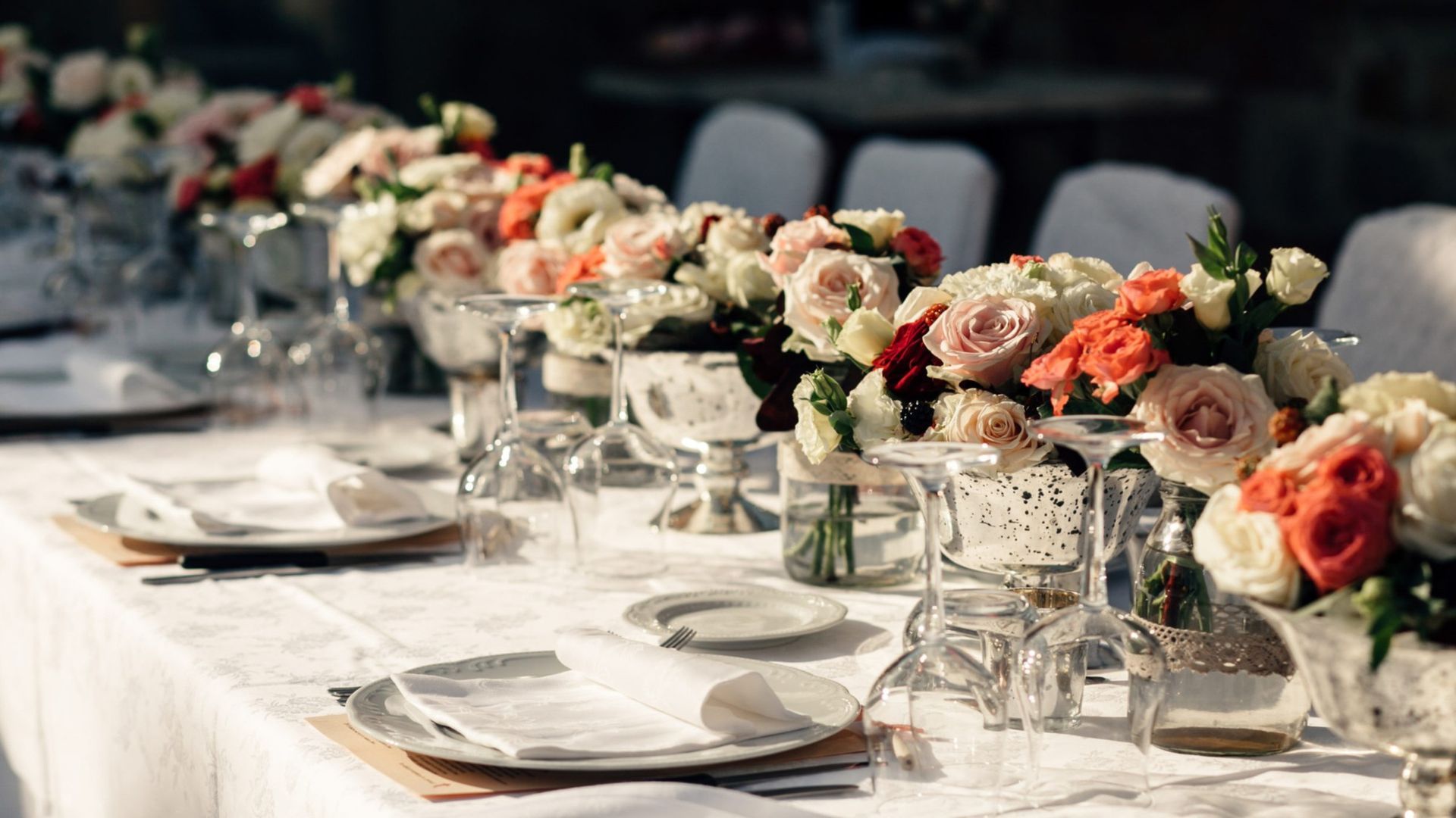 Elegant banquet table with white plates, glassware, and low pink-and-white floral centerpieces