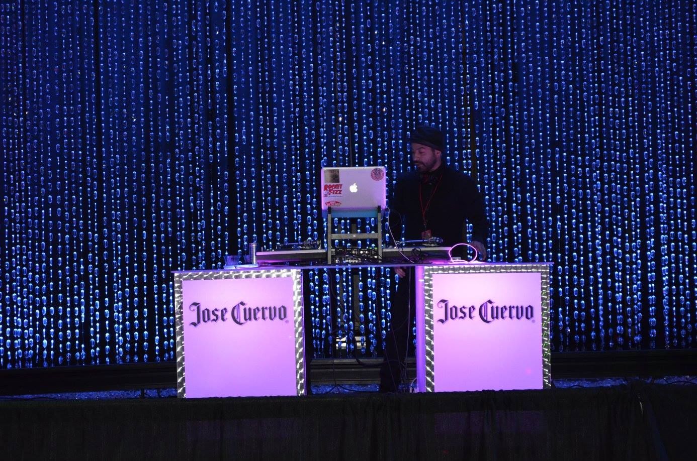 DJ performing behind two lit “Jose Cuervo” tables on a dark stage with blue LED backdrop