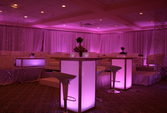 Purple-lit banquet room with cocktail tables, glowing columns, and draped curtains