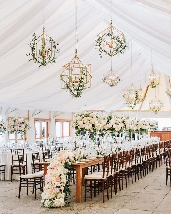 Elegant tented wedding reception with long decorated tables, white florals, and hanging geometric chandeliers