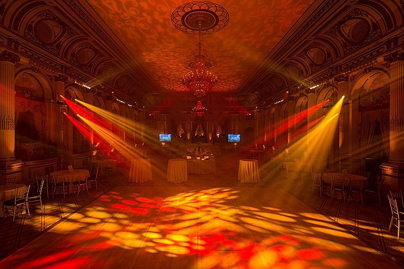 Empty ornate ballroom lit by red and gold stage lights, with patterned light on the floor