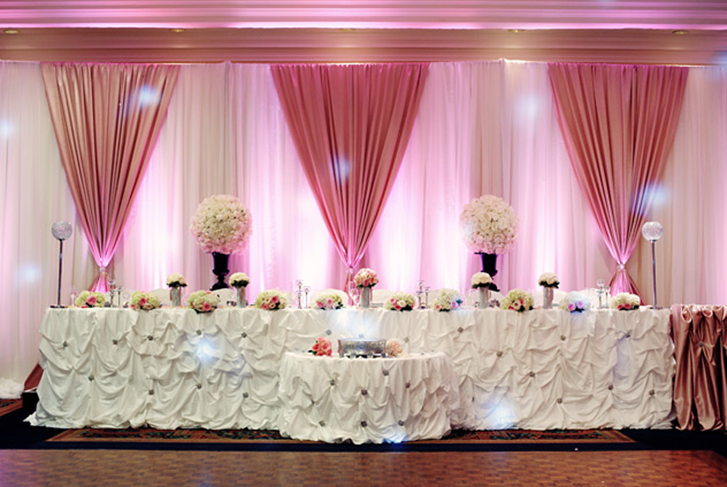 Pink-lit banquet table with white floral centerpieces, draped curtains, and white rosette tablecloths