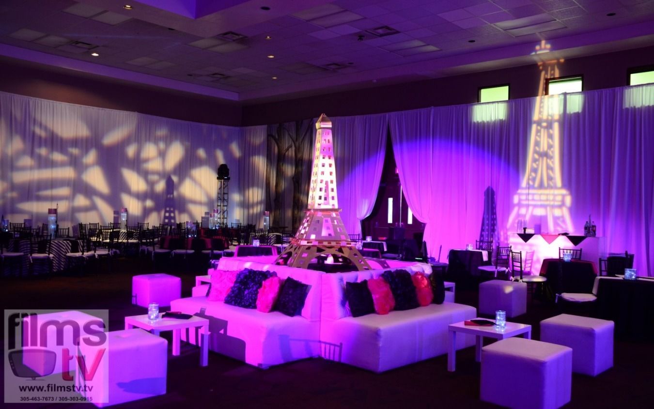 Purple-lit event lounge with white seating and Eiffel Tower decor on a stage-like platform