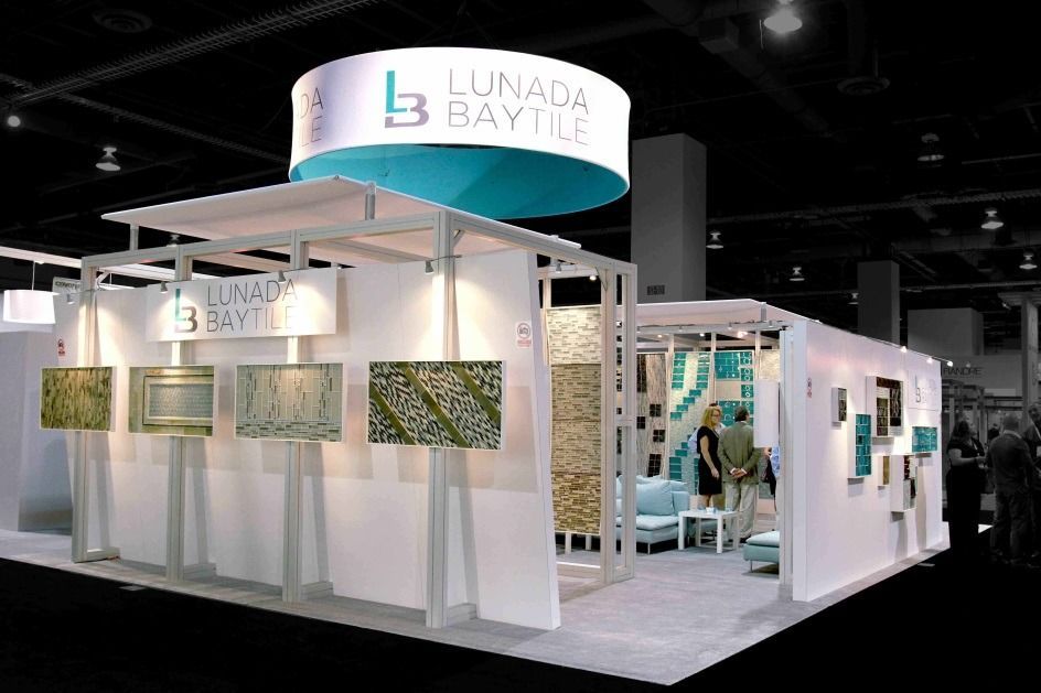 White trade show booth with curved overhead signs and green display panels in a convention hall