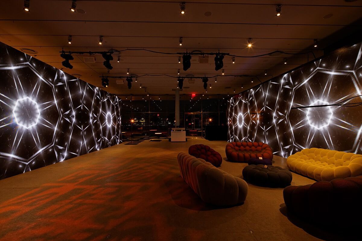 Dim lounge with glowing circular wall lights, warm orange carpet, and low seating benches.