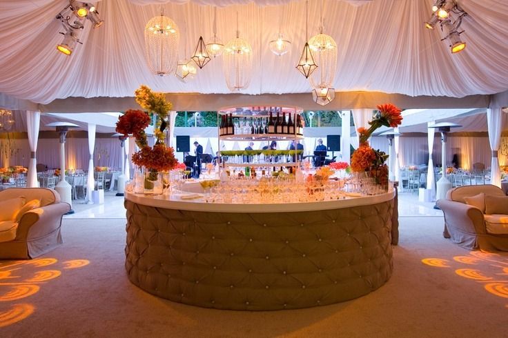 Elegant white wedding reception tent with a circular bar, chandeliers, and warm ambient lighting