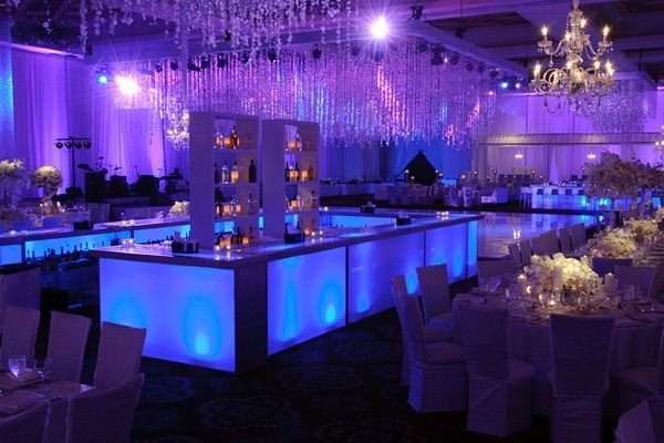 Purple-lit banquet hall with a glowing bar, chandeliers, and set dining tables