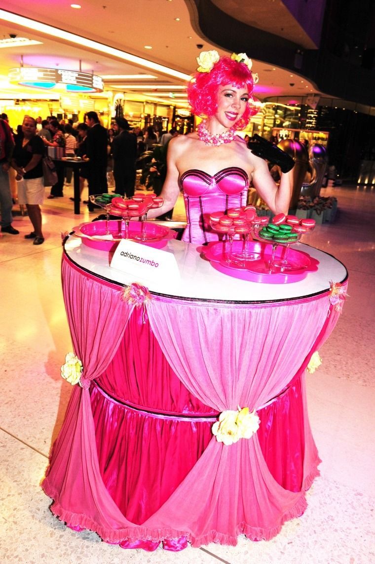 Person in bright pink costume standing behind a decorated pink display table at an indoor event.