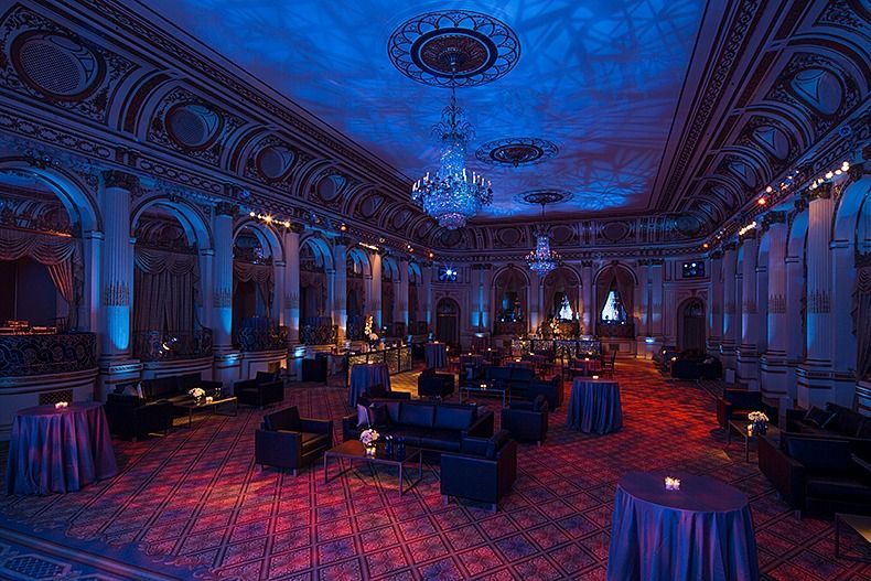 Elegant banquet hall with blue and red lighting, ornate columns, and scattered tables and chairs