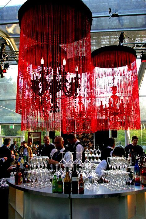 Red beaded chandeliers above a crowded bar with glassware and people mingling indoors