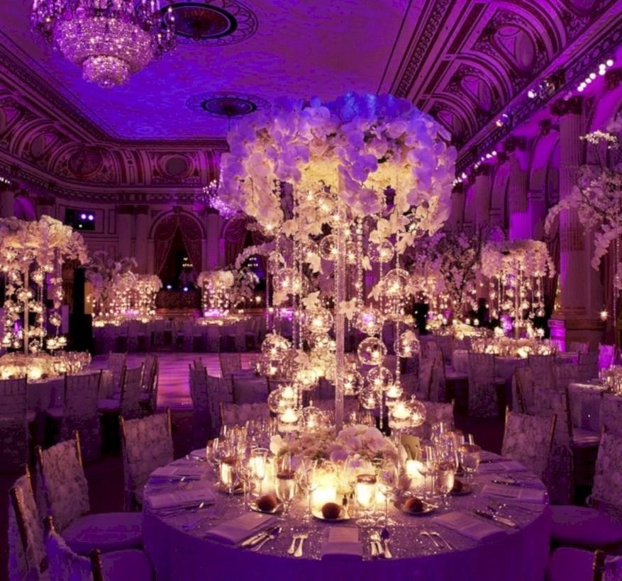 Purple-lit ornate banquet hall with tall floral centerpieces and candlelit round tables